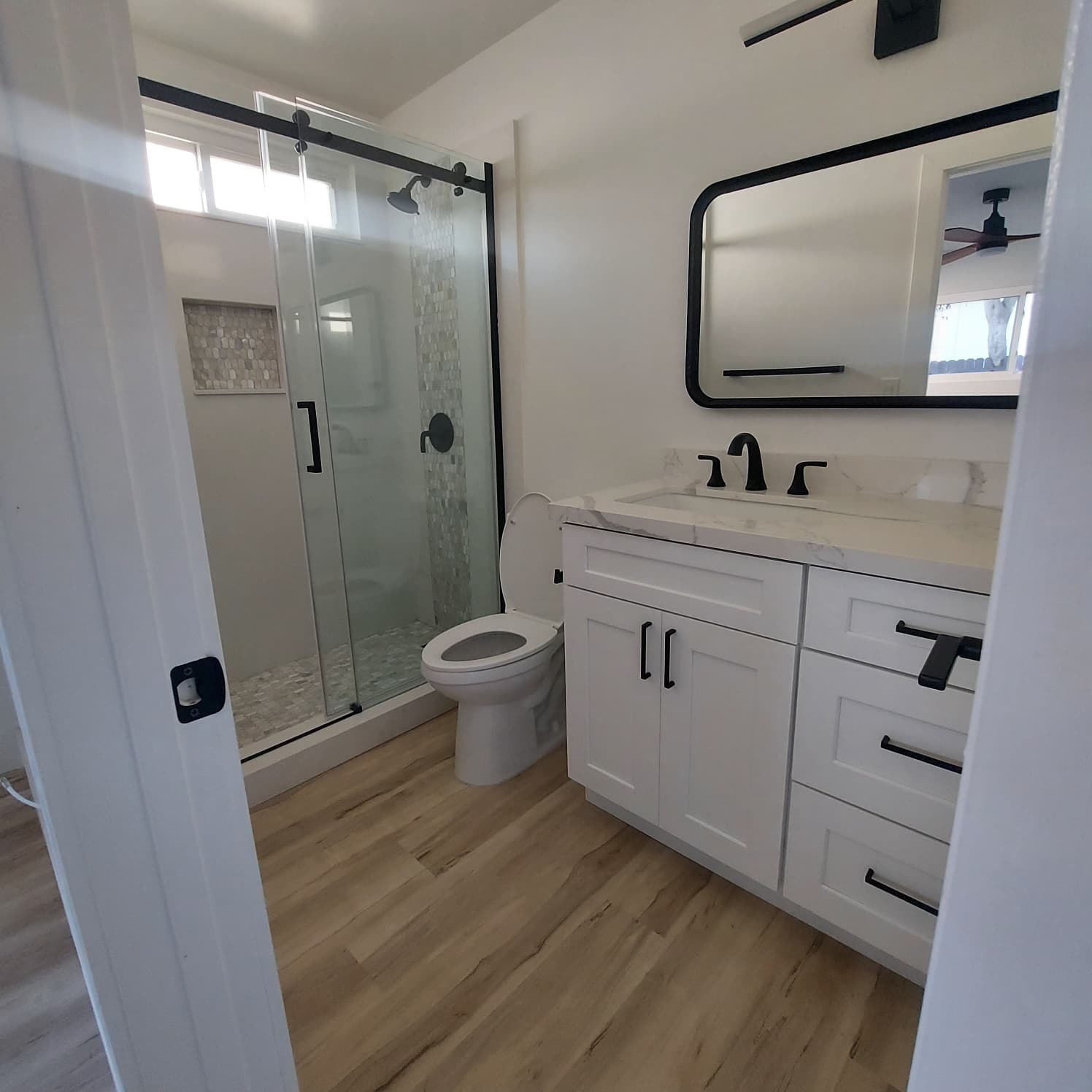 Complete bathroom remodel with white shaker vanity, quartz countertop, frameless glass shower enclosure, and matte black hardware