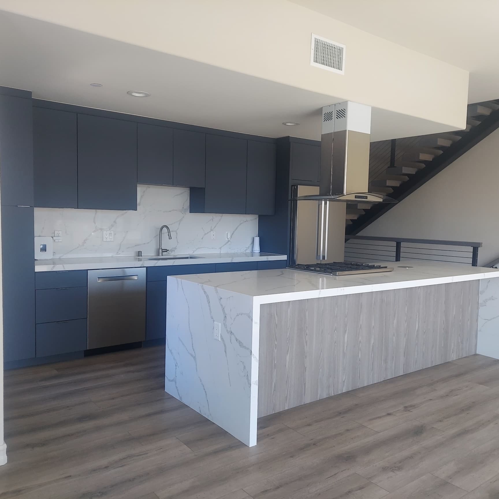 Modern kitchen remodel with navy blue flat-front cabinets, calacatta marble waterfall island, and matching marble backsplash